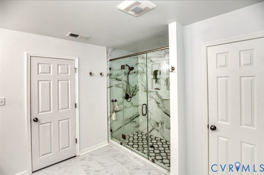 13501 Cooks Mill Court, Cooks Mill, Lanexa, VA 23089 Walk-in glass shower enclosure featuring large-format stone-patterned wall tile, integrated recessed shelving, patterned tile flooring, and matte black hardware