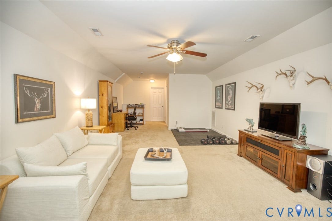 13501 Cooks Mill Court, Cooks Mill, Lanexa, VA 23089 Neutral-toned interior space featuring carpeted flooring, a multi-blade ceiling fan, slanted ceiling architecture, and a central white six-panel door