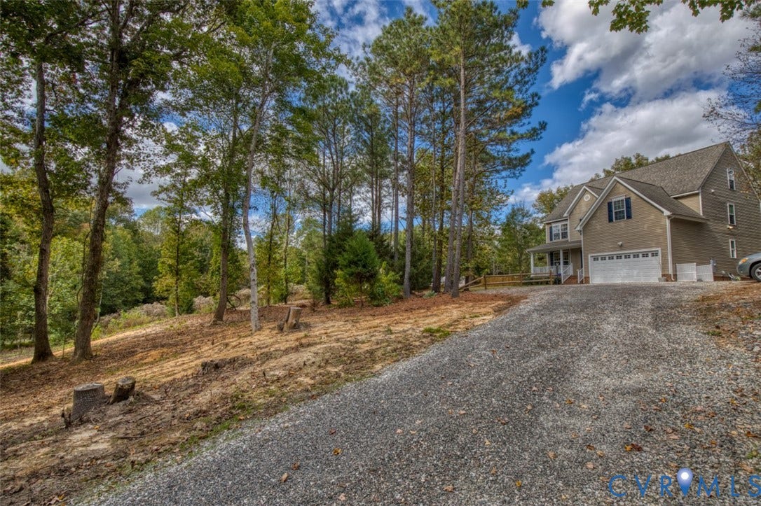 13501 Cooks Mill Court, Cooks Mill, Lanexa, VA 23089 Multi-story residence featuring a shingled roof, neutral-toned siding, a two-car garage, and a private gravel driveway nestled within a wooded lot