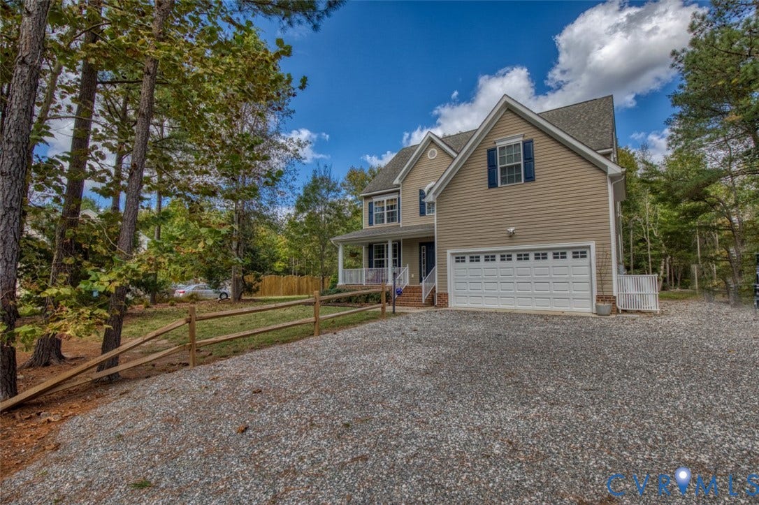 13501 Cooks Mill Court, Cooks Mill, Lanexa, VA 23089 Two-story residential exterior featuring neutral vinyl siding, a two-car garage, shuttered windows, and a covered front porch with a white railing