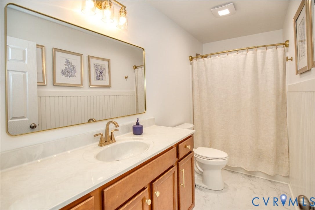 13501 Cooks Mill Court, Cooks Mill, Lanexa, VA 23089 Bathroom featuring a vanity with a light-toned countertop, beadboard wainscoting, a large brass-framed vanity mirror, brass-finish faucet hardware, and a matching brass shower curtain rod
