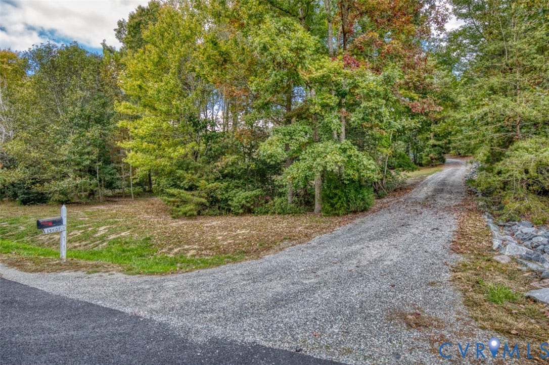 13501 Cooks Mill Court, Cooks Mill, Lanexa, VA 23089 Gravel driveway entry featuring mature trees, wooded perimeter, and stone edging