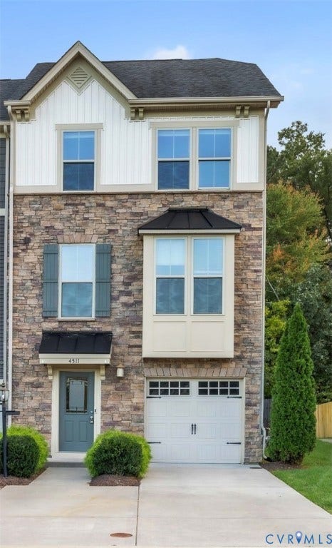 4511 Wistar Woods Trail, Richmond, VA 23228 Three-story exterior featuring multi-toned stone masonry, vertical board-and-batten siding, a metal-accented bay window, and a carriage-style garage door