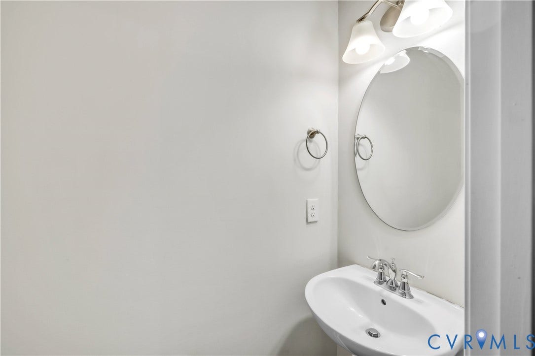 4511 Wistar Woods Trail, Richmond, VA 23228 Wall-mounted oval mirror, pedestal sink with chrome dual-handle faucet, and three-light vanity fixture