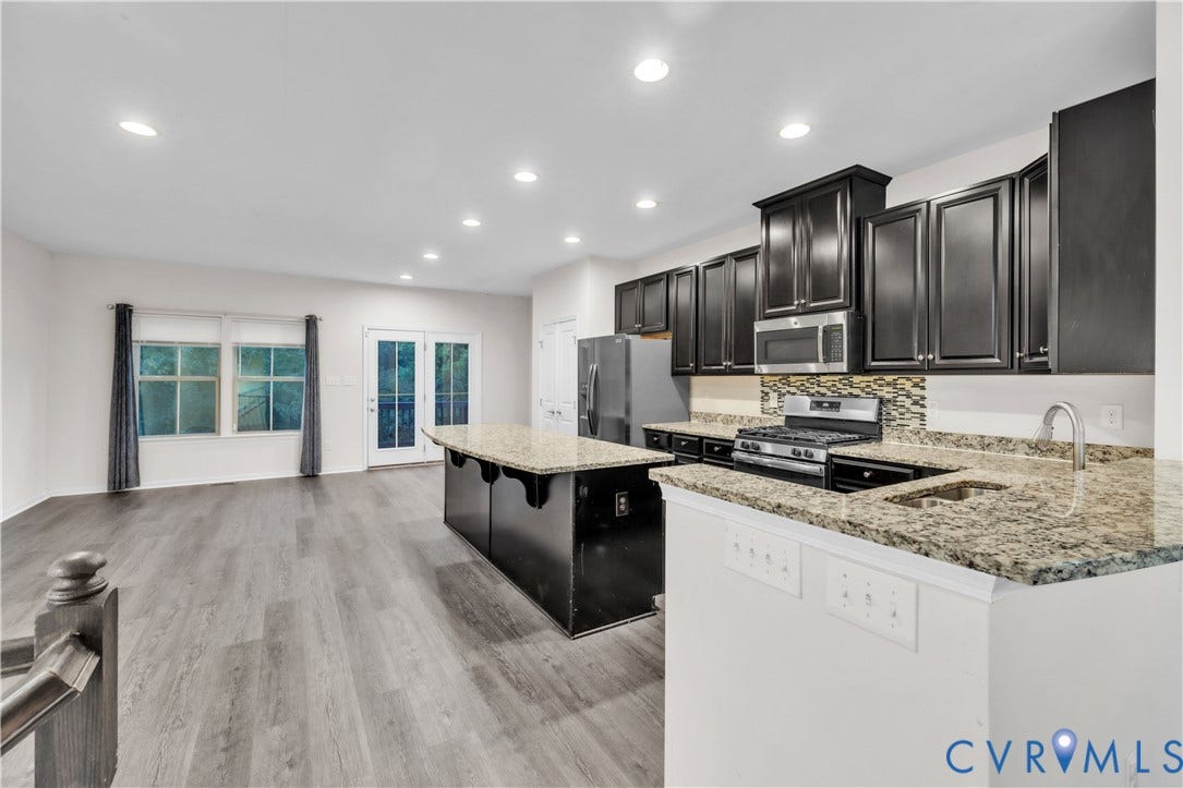 4511 Wistar Woods Trail, Richmond, VA 23228 Kitchen featuring dark cabinetry, stone countertops, integrated stainless steel appliances, a center island with seating space, and wood-finish flooring