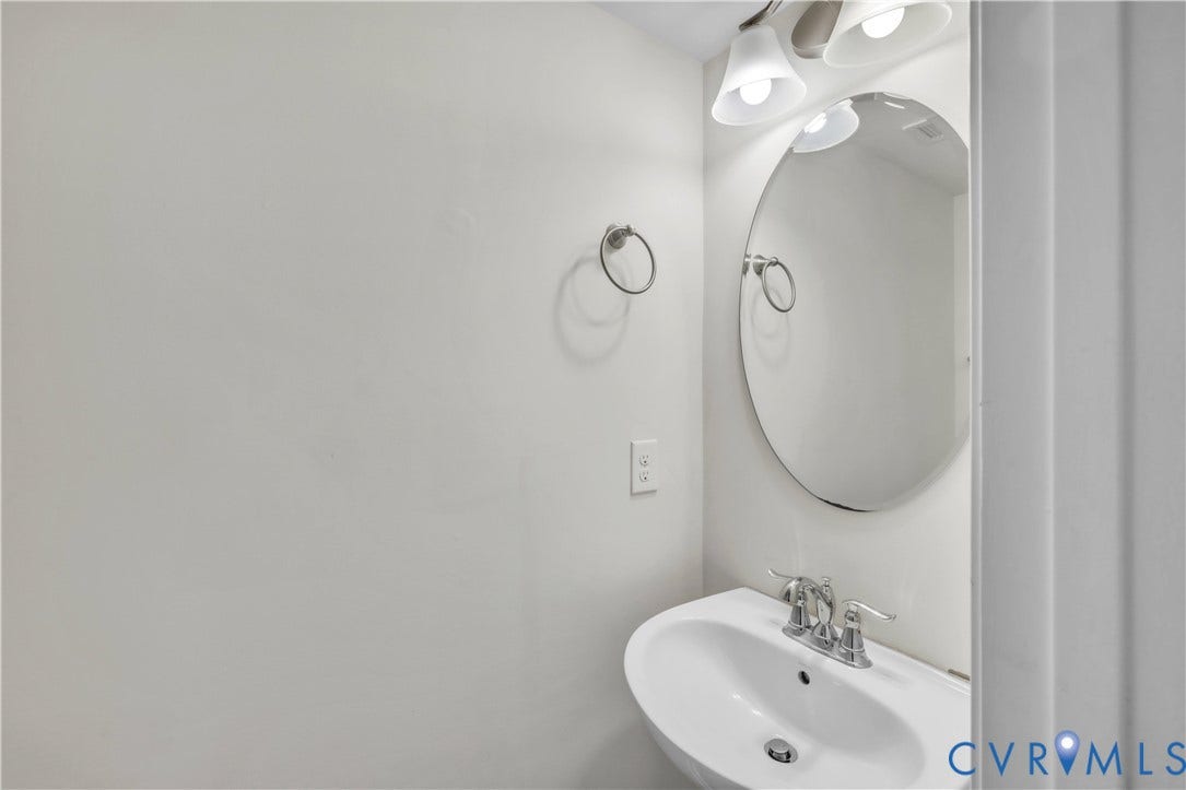 4511 Wistar Woods Trail, Richmond, VA 23228 Oval wall-mounted mirror featuring a polished metal finish, pedestal sink with a dual-handle chrome faucet, and multi-bulb vanity light fixture