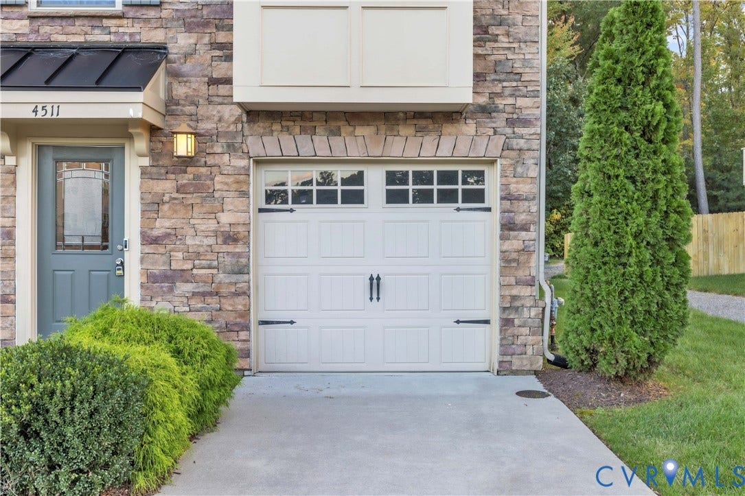 4511 Wistar Woods Trail, Richmond, VA 23228 Exterior faade featuring stone veneer siding, an attached garage with window-pane detailing and decorative hardware, a metal roof accent, and a solid entry door with a glass insert