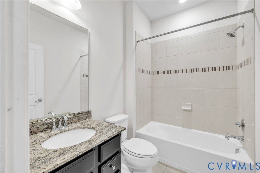 4511 Wistar Woods Trail, Richmond, VA 23228 Bathroom featuring a dark wood-finish vanity, stone-patterned countertop, oval under-mount sink, and a shower-tub combination with decorative tile inlay