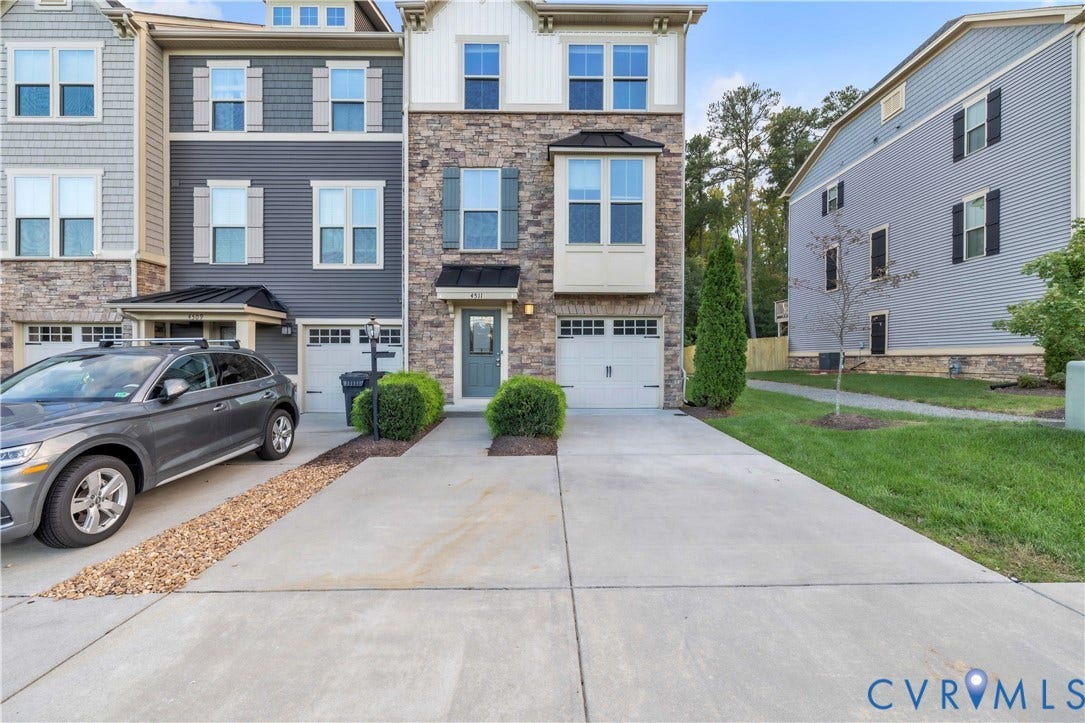 4511 Wistar Woods Trail, Richmond, VA 23228 Three-story townhome exterior featuring stone veneer facade, vertical board-and-batten siding, metal roof accents, and concrete driveway