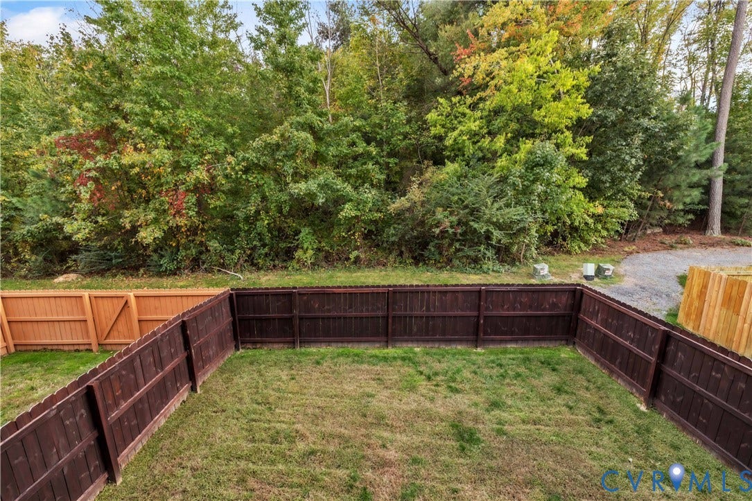 4511 Wistar Woods Trail, Richmond, VA 23228 Rear yard enclosed by dark-stained wood privacy fencing, featuring a grass lawn and direct border to dense mature tree lines