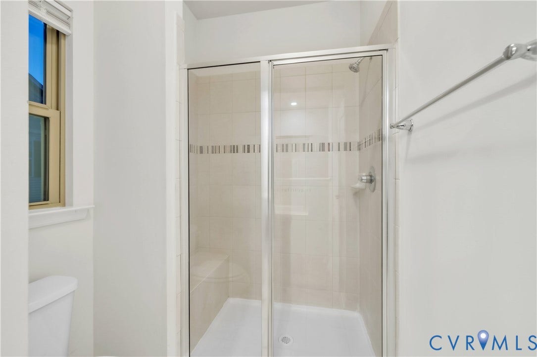 4511 Wistar Woods Trail, Richmond, VA 23228 Walk-in shower featuring a glass sliding enclosure, tile wall surround with decorative inlay, built-in bench seating, and polished metal fixtures