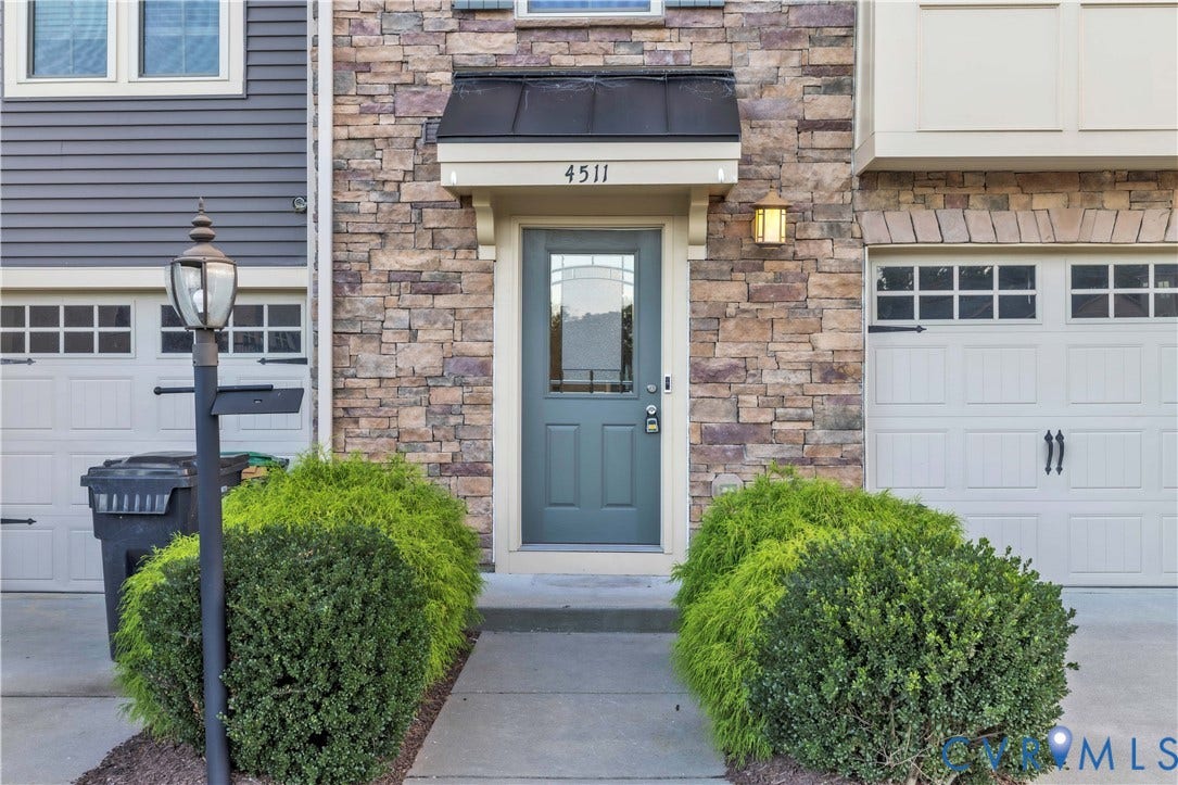 4511 Wistar Woods Trail, Richmond, VA 23228 Exterior facade featuring multi-tonal masonry veneer, a dark metal door awning, a paneled entry door with an arched glass insert, and two carriage-style garage doors