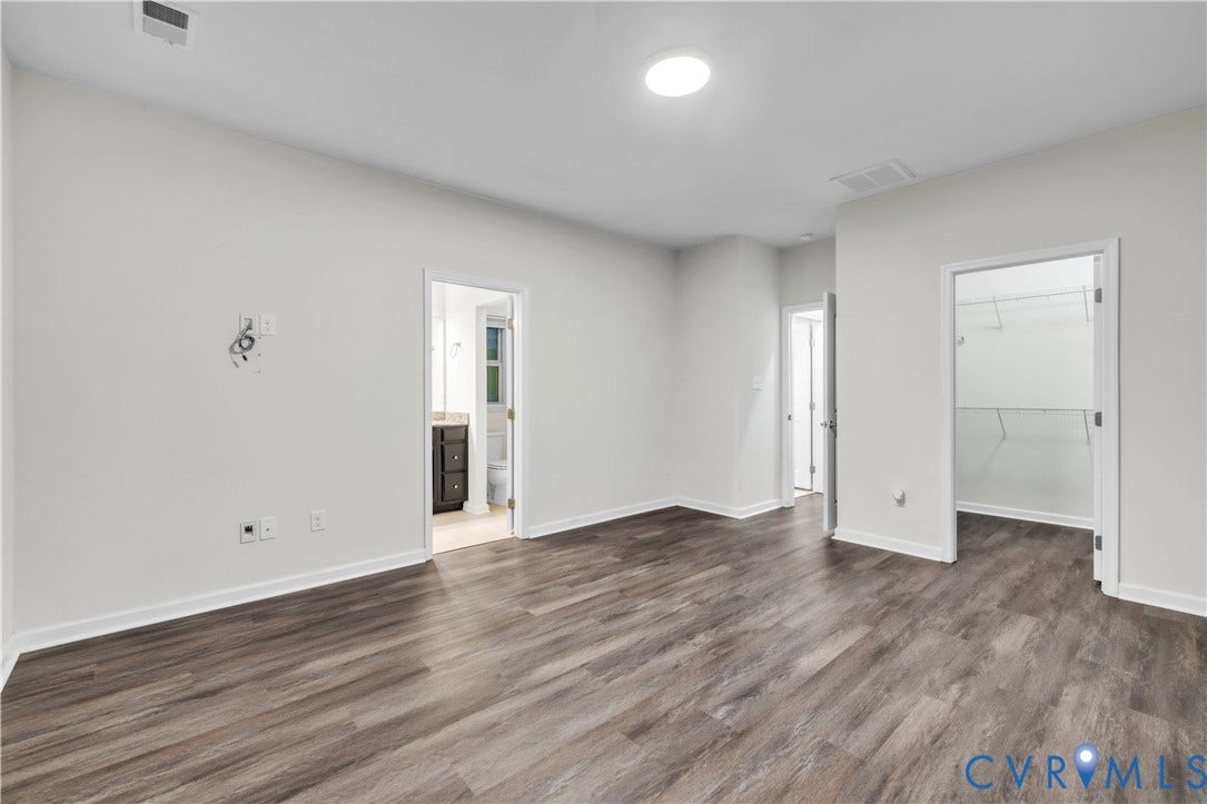 4511 Wistar Woods Trail, Richmond, VA 23228 Neutral-toned interior space featuring wood-finish flooring, flush-mount ceiling lighting, and two interior doorways leading to an en-suite area and a walk-in closet with built-in shelving