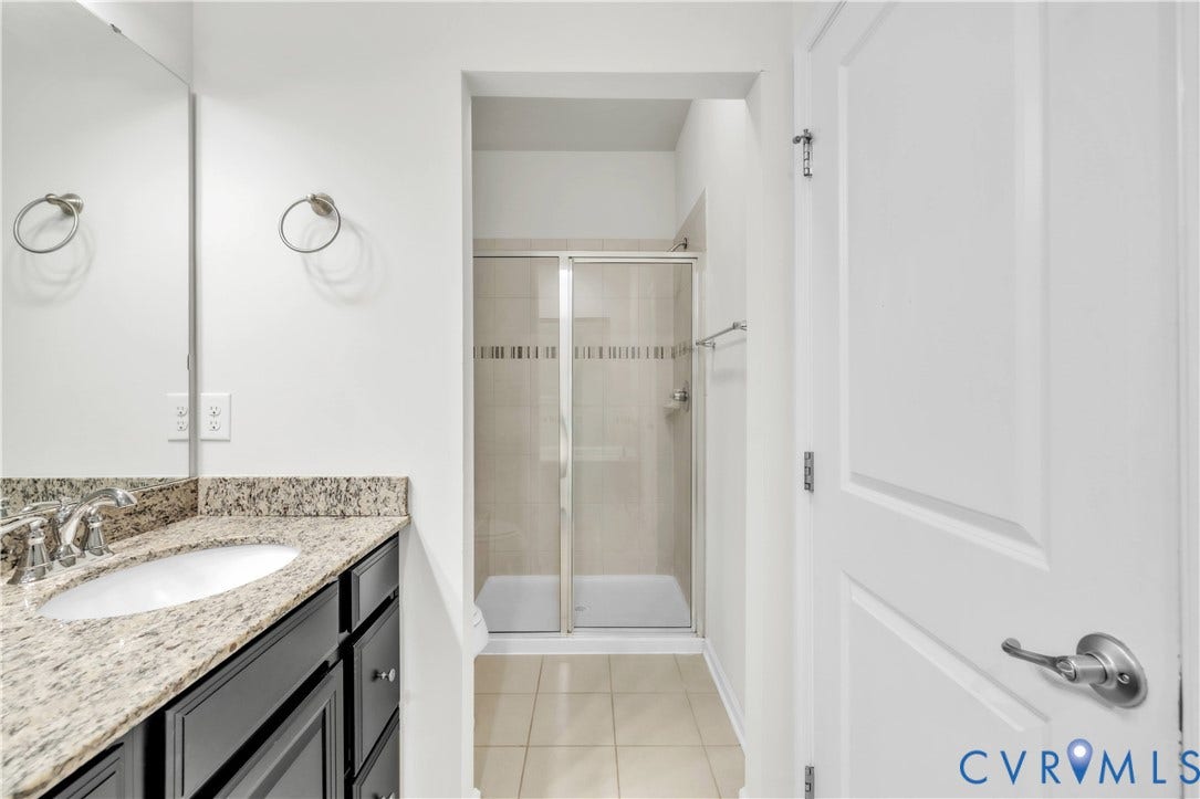 4511 Wistar Woods Trail, Richmond, VA 23228 Bathroom featuring a vanity with stone-finish countertop, undermount sink, and dark cabinetry, paired with a glass-enclosed shower with tile surround and tile flooring
