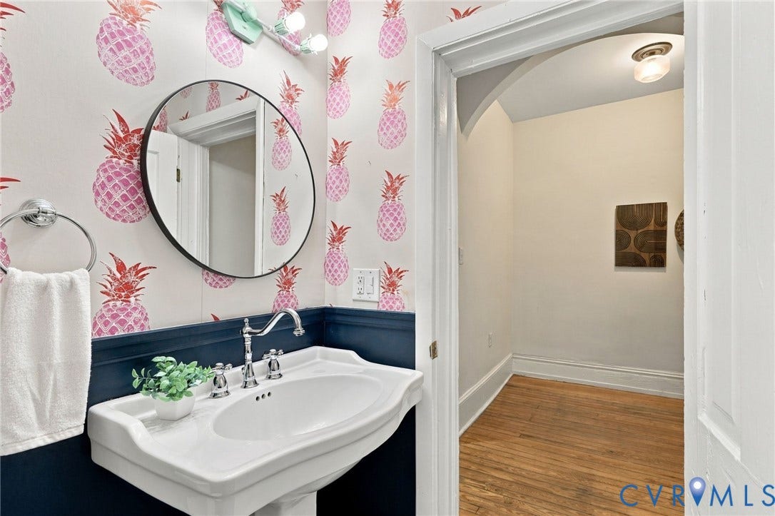 522 N 27th Street, Church Hill, Richmond, VA 23223 Wall-mounted pedestal sink with chrome faucet, circular wall mirror, custom patterned wallpaper, and navy blue wainscoting