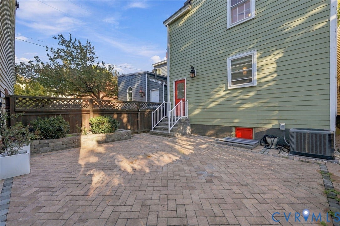522 N 27th Street, Church Hill, Richmond, VA 23223 Rear exterior featuring a herringbone-pattern paver patio, wood lattice privacy fencing, stone retaining wall, and horizontal siding