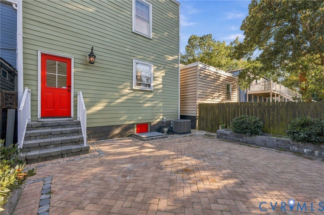 522 N 27th Street, Church Hill, Richmond, VA 23223 Exterior featuring horizontal lap siding, a paved brick patio, stone-block steps, a red entry door, and a wood privacy fence