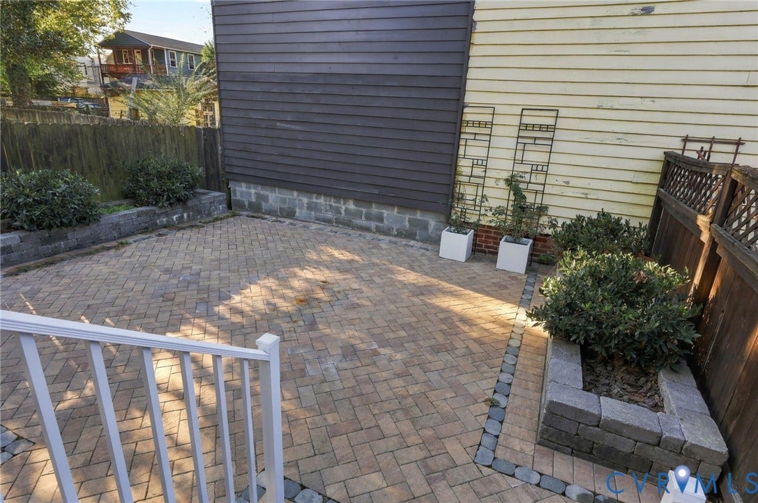 522 N 27th Street, Church Hill, Richmond, VA 23223 Herringbone-patterned paver patio featuring raised stone planters, a wood privacy fence, and metal decorative trellises