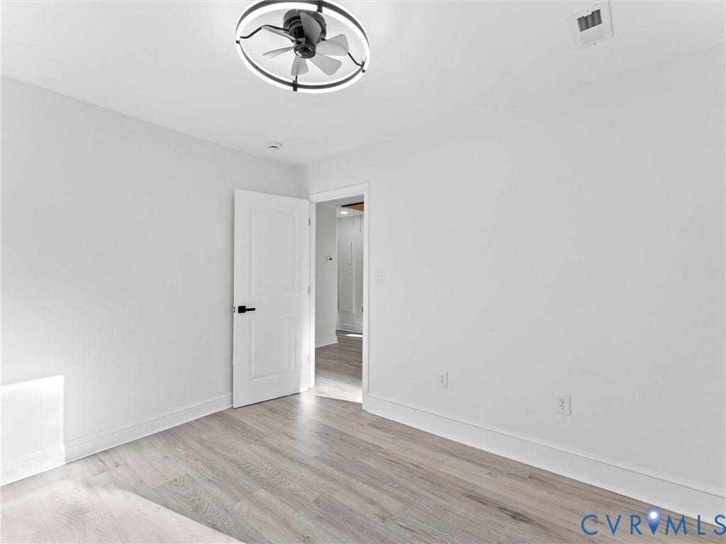 135 Elm Street, Petersburg, VA 23803 Interior room featuring wood-finish flooring, a modern circular LED ceiling fan, and a single-panel interior door with matte black hardware