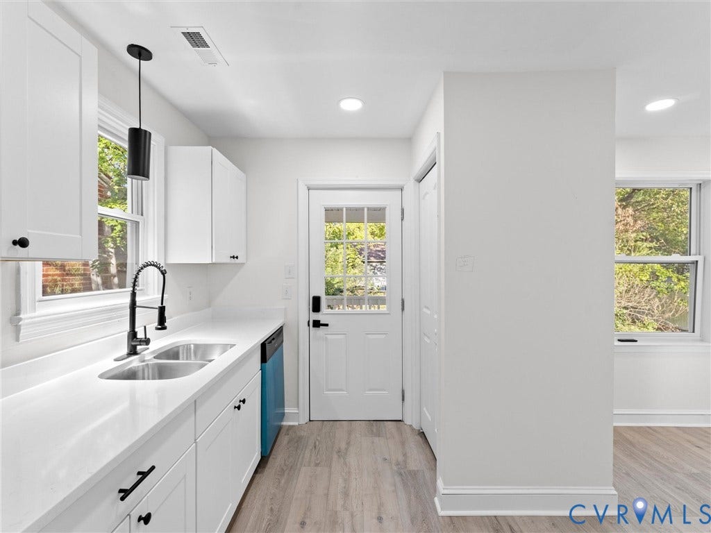 135 Elm Street, Petersburg, VA 23803 Kitchen area featuring white shaker-style cabinetry, solid-surface countertops, dual-basin stainless steel sink with a matte black faucet, and wood-finish flooring