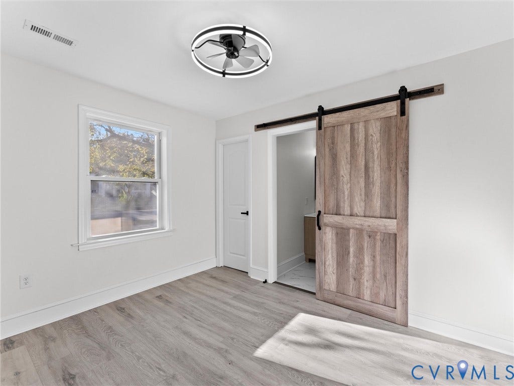 135 Elm Street, Petersburg, VA 23803 Interior space featuring wood-finish flooring, a sliding barn door with matte black hardware, and a modern circular ceiling fan with integrated lighting