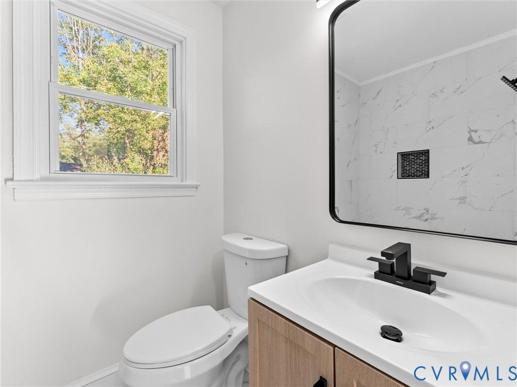 135 Elm Street, Petersburg, VA 23803 Bathroom featuring a wood-finish vanity with a white countertop, matte black faucet, framed mirror, and tile shower surround with a built-in niche