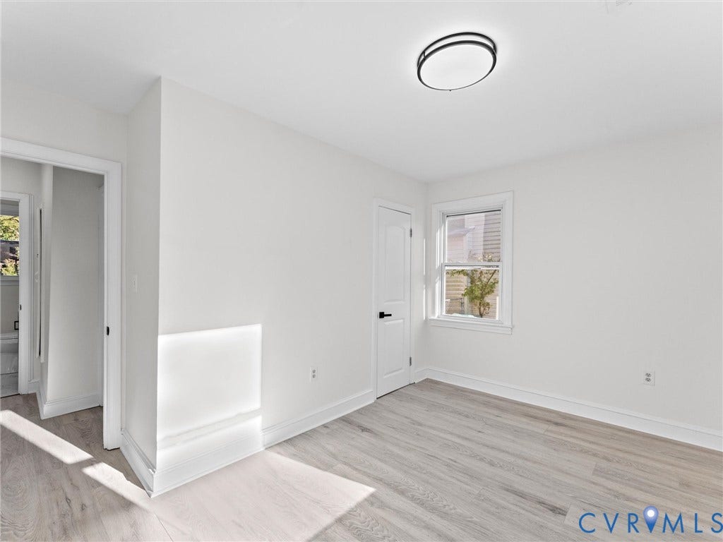 135 Elm Street, Petersburg, VA 23803 Interior room featuring wood-finish flooring, a neutral color palette, a single-hung window, a modern circular flush-mount ceiling light, and a six-panel door with matte black hardware