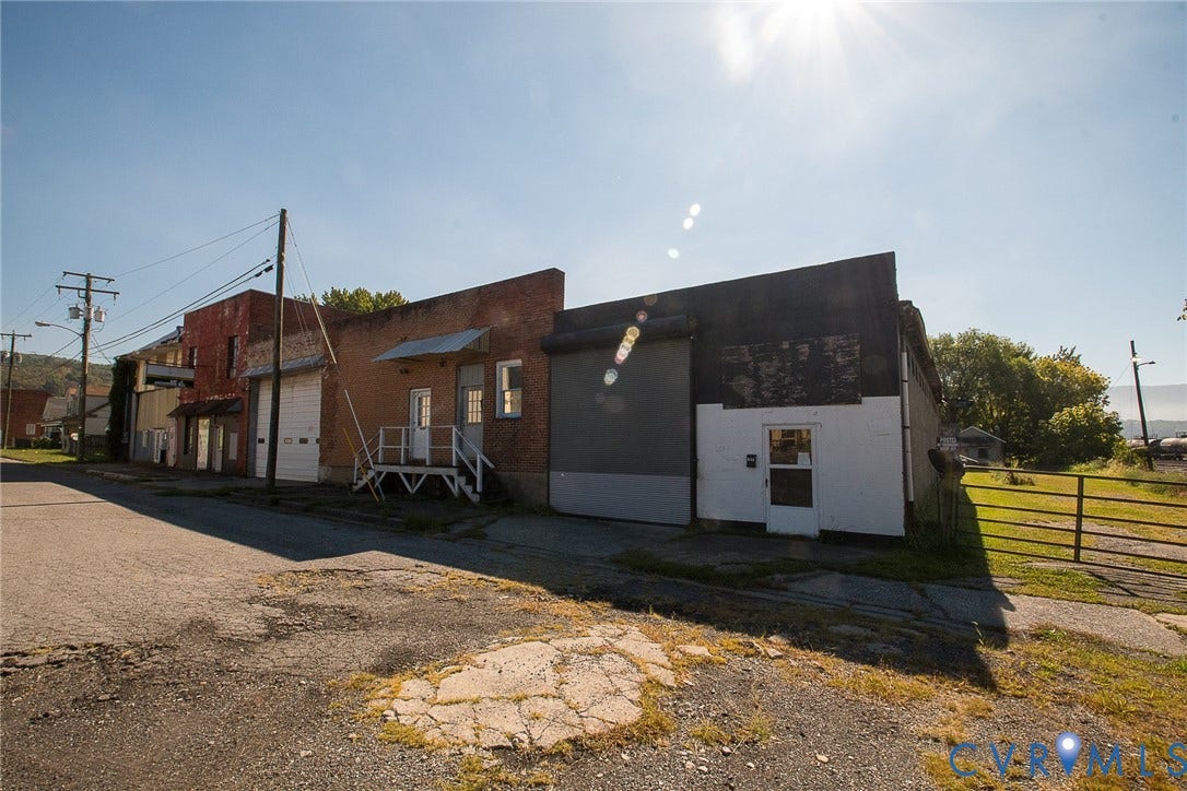 109 E Oak Street, Covington, VA 24426 Mixed-use structure featuring brick and masonry exterior, metal rolling bay doors, elevated metal entryway steps, and gated perimeter access