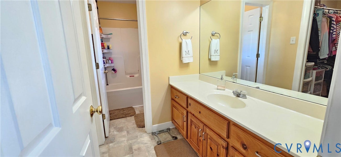 8605 Howerton Road, Center Cross, VA 22437 Bathroom featuring a vanity with wood cabinetry, a solid-surface countertop with an integrated sink, a large wall-mounted mirror, and a tub-shower combination with a surround
