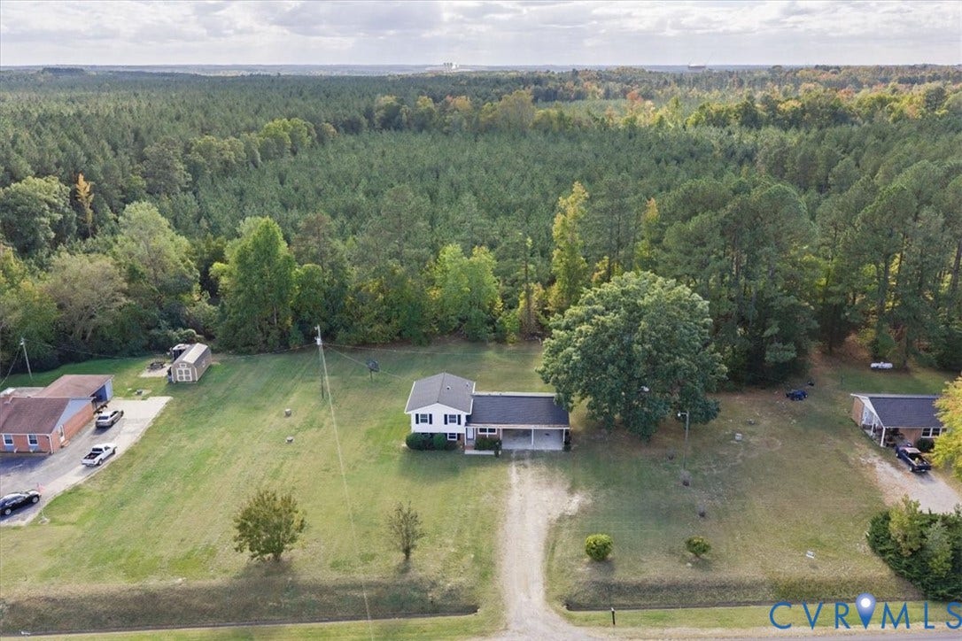 4942 Pleasant Shade Drive, Emporia, Emporia, VA 23847 Aerial perspective of a detached residence featuring a covered carport, an expansive lawn, and mature trees, set against a backdrop of dense woodland