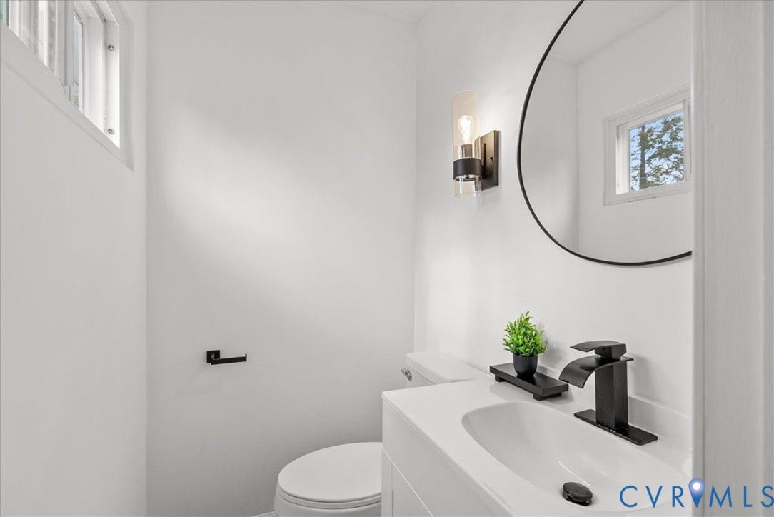 4942 Pleasant Shade Drive, Emporia, Emporia, VA 23847 White vanity with a solid surface countertop, undermount sink, matte black widespread faucet, oval mirror, and a wall-mounted cylinder light fixture