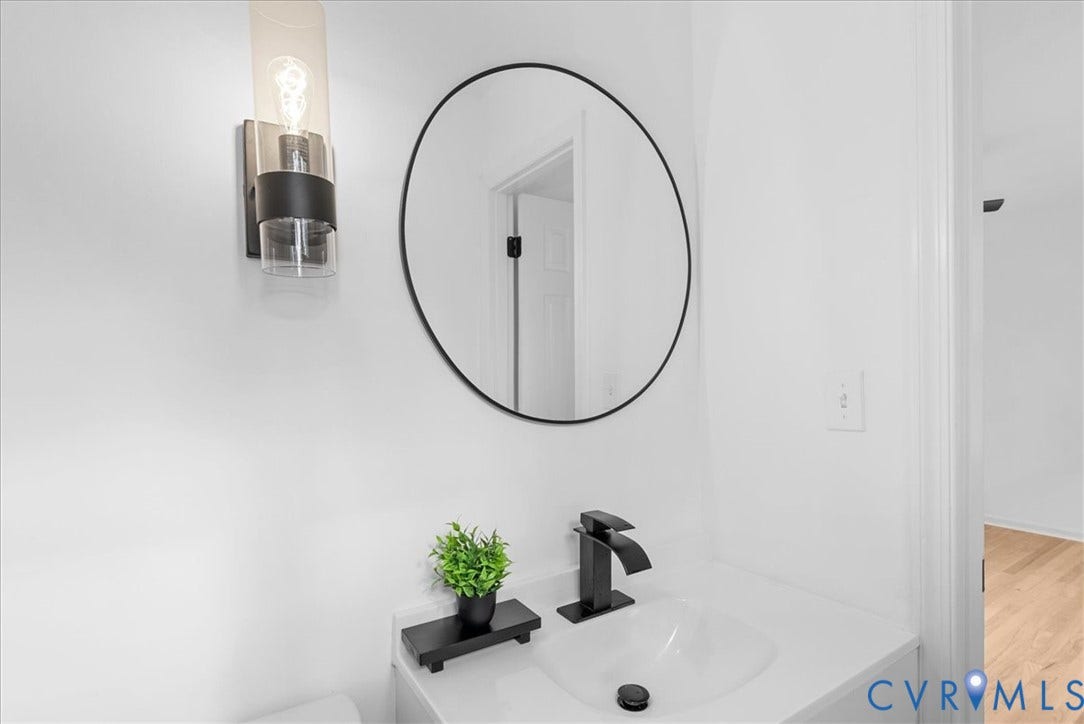 4942 Pleasant Shade Drive, Emporia, Emporia, VA 23847 Wall-mounted cylindrical glass and matte black sconce, circular mirror with a slim black frame, integrated vanity countertop with an undermount basin, and matte black single-handle faucet