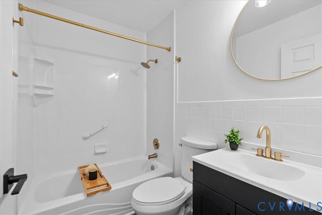 4942 Pleasant Shade Drive, Emporia, Emporia, VA 23847 Bathroom featuring a dark-finish vanity with an integrated white countertop, brass-tone hardware, a circular mirror with a matching metallic frame, and a white tub-and-shower enclosure with square wall tile detailing