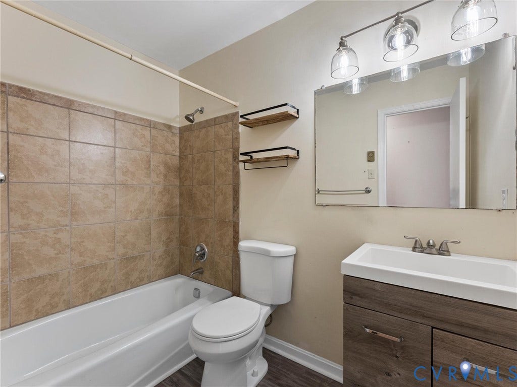 503 Briarwood Circle, Jefferson Circle, North Prince George, VA 23860 Bathroom featuring a wood-finish vanity with a rectangular sink, wall-mounted light fixture, large vanity mirror, built-in shelving, and a tub enclosure with neutral-toned tiling
