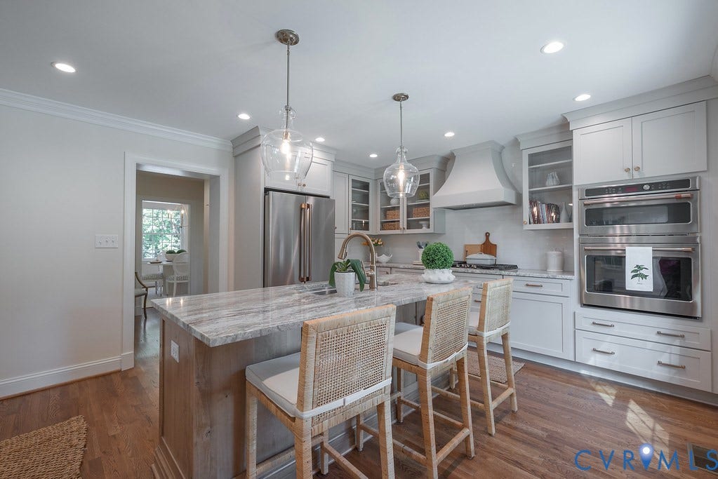 Kitchen featuring stone-surface island with integrated sink, wood-finish flooring, custom cabinetry with glass-front accents, stainless steel double wall ovens, and recessed lighting