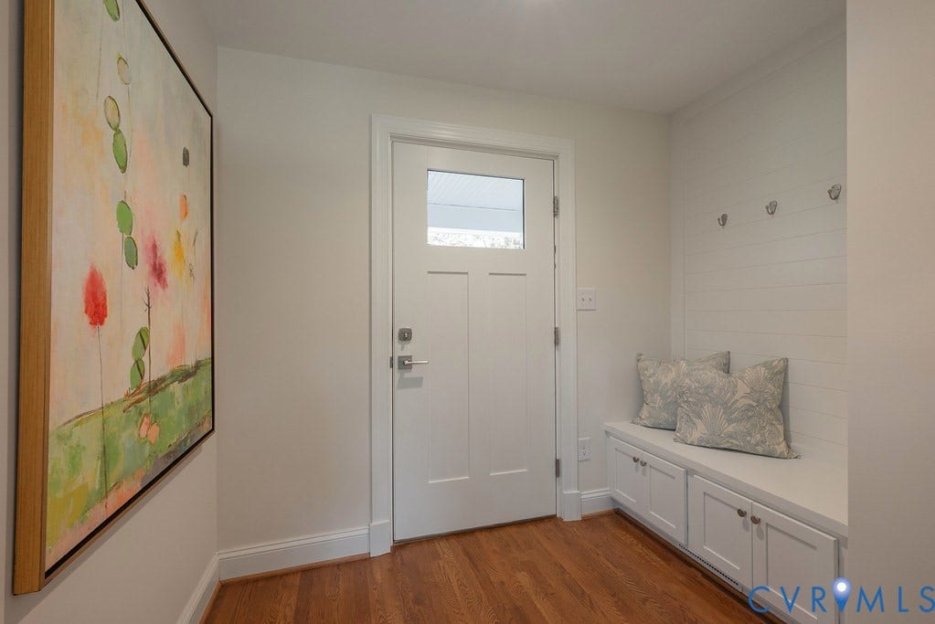 Entryway featuring wood-finish flooring, a white exterior door with an inset glass panel, built-in cabinetry with bench seating, and wall-mounted shiplap detailing with metal hooks