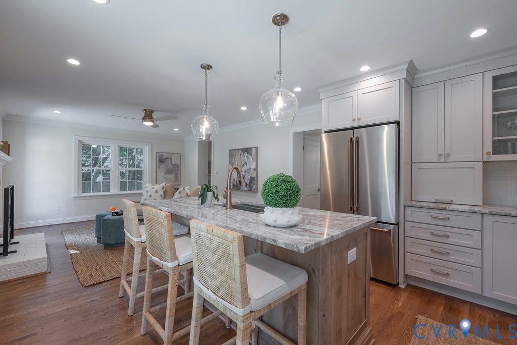 Kitchen featuring a stone-surface island, wood-finish cabinetry with crown molding, stainless steel refrigerator, glass pendant lighting, and wood-finish flooring