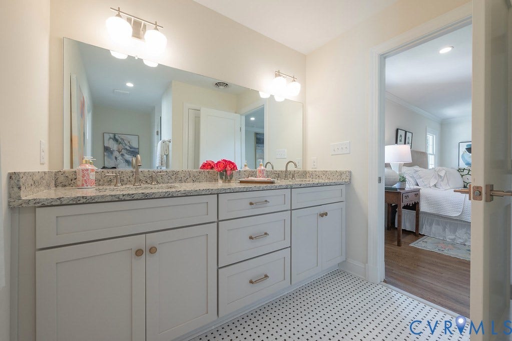 Dual-sink vanity with light-tone cabinetry, stone-finish countertops, wall-to-wall mirror, and geometric mosaic tile flooring