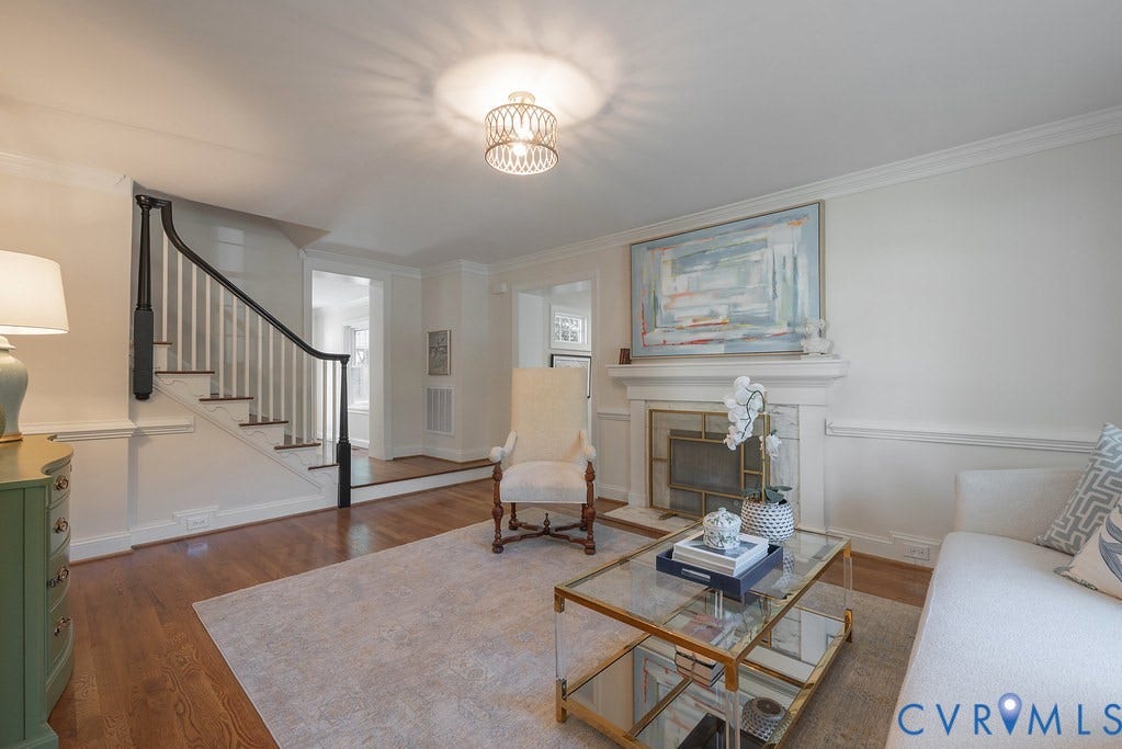 Living space featuring wood-finish flooring, a fireplace with a decorative mantel, crown molding, chair rail trim, and a staircase with a dark-finished handrail and balusters