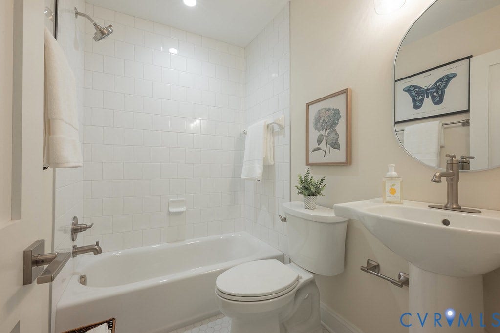 Bathroom featuring a shower-tub combination with white subway tile surround, pedestal sink with metallic faucet, and a circular wall-mounted mirror