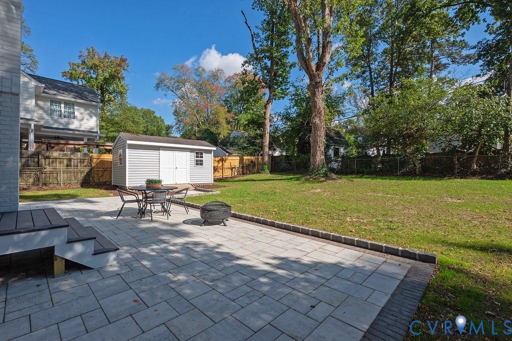 Backyard featuring a paved stone patio, a detached storage shed, a lawn, perimeter fencing, and mature trees