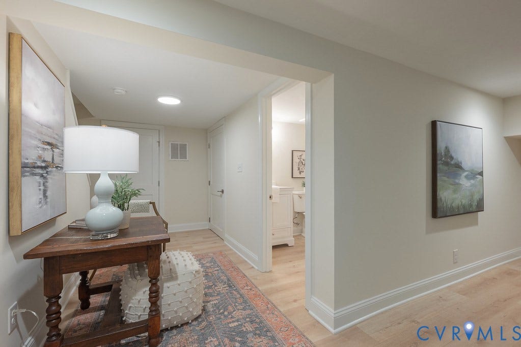 Neutral interior hallway featuring light-toned wood-finish flooring, recessed ceiling lighting, and solid-core paneled doors