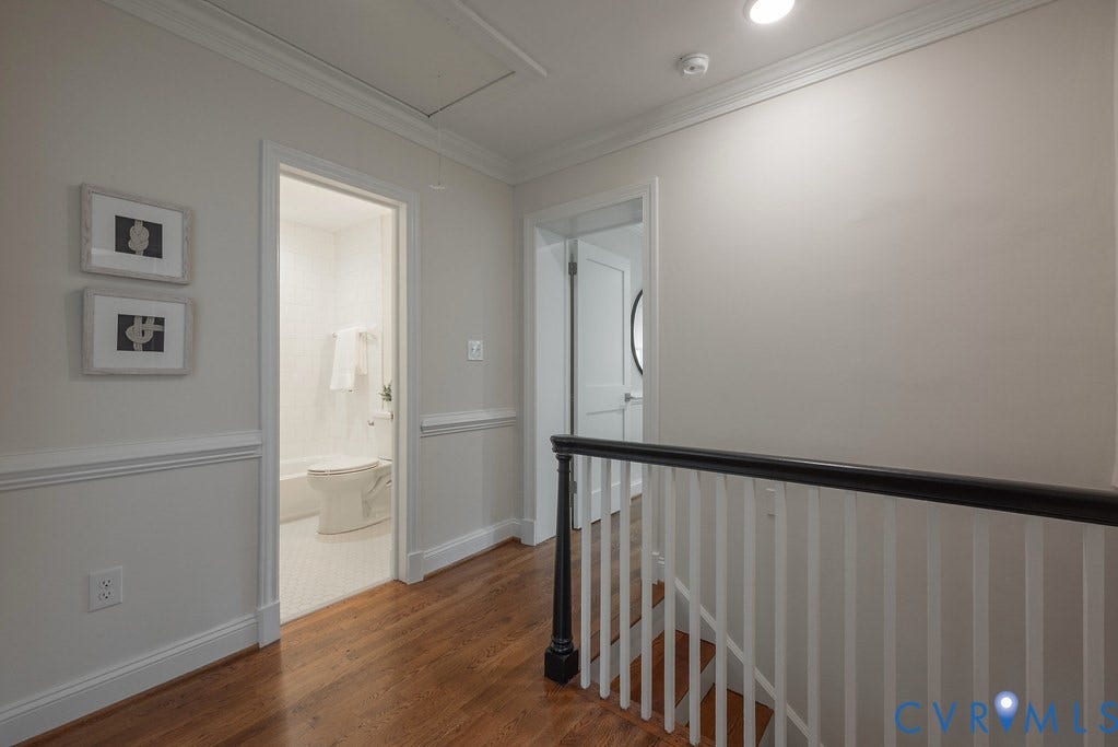 Interior hallway featuring wood-finish flooring, white chair rail molding, crown molding, and a staircase with a dark-toned handrail and white balusters
