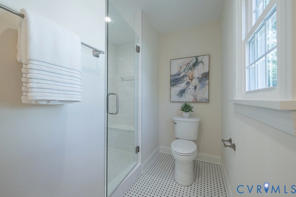 Bathroom featuring a glass-enclosed shower with tiled surround and built-in bench, geometric patterned floor tile, and double-hung window