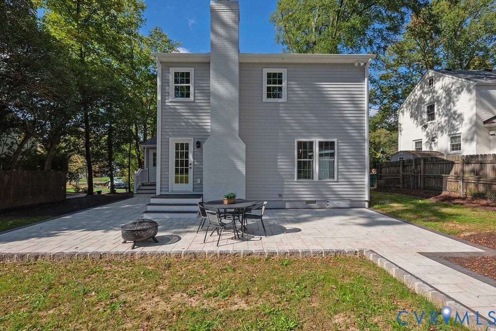 Exterior featuring light-gray horizontal siding, a prominent brick chimney, and a sprawling paver patio with a stone border