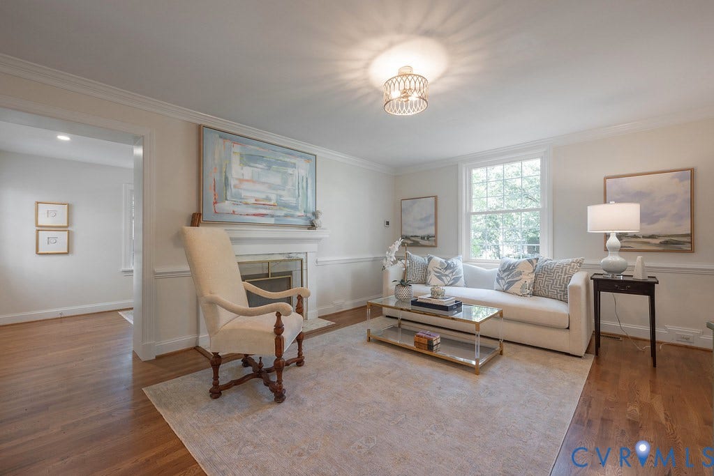 Living area featuring wood-finish flooring, a wood-burning fireplace with a mantel, chair rail molding, crown molding, and a multi-pane window