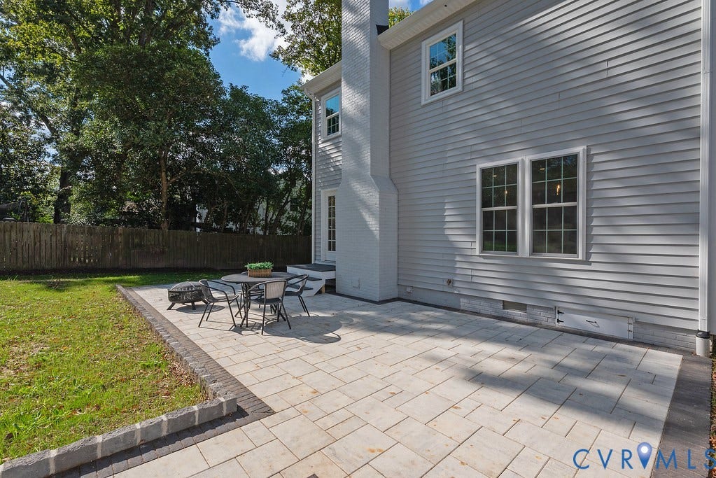 Rear exterior featuring light grey siding, a white painted brick chimney, and a stone paver patio with a decorative border