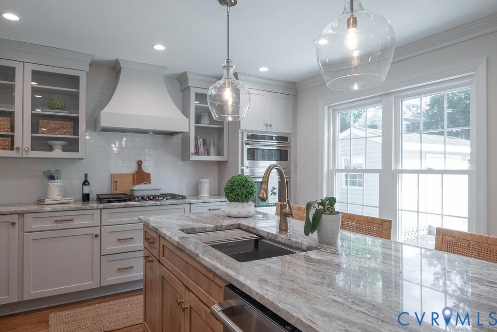 Kitchen featuring an island with stone-finish countertops, stainless steel undermount sink, custom cabinetry, glass-front upper storage, and built-in stainless steel appliances