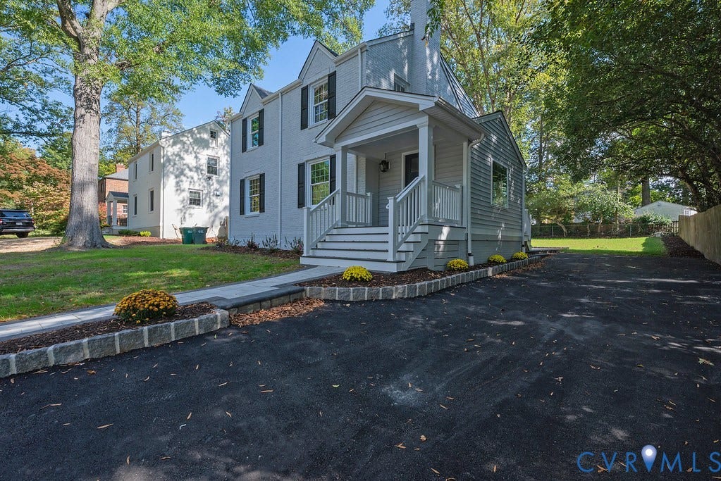 Two-story residence featuring a painted brick exterior, a covered entryway with white railings, black shutters, and an asphalt driveway