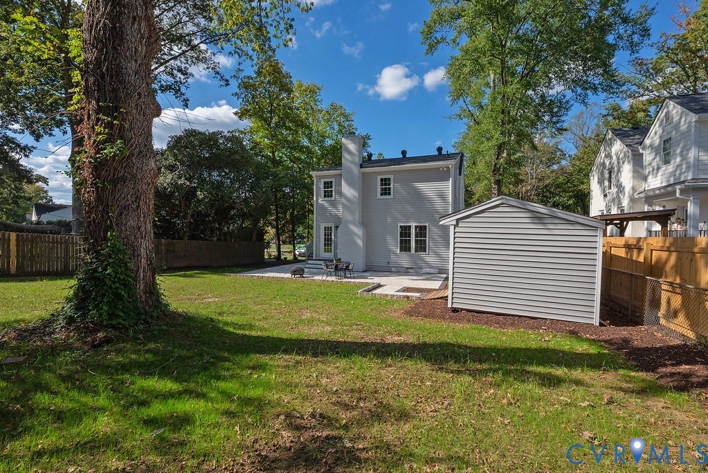 Expansive backyard featuring a manicured lawn, stone patio, detached storage structure, and perimeter privacy fencing
